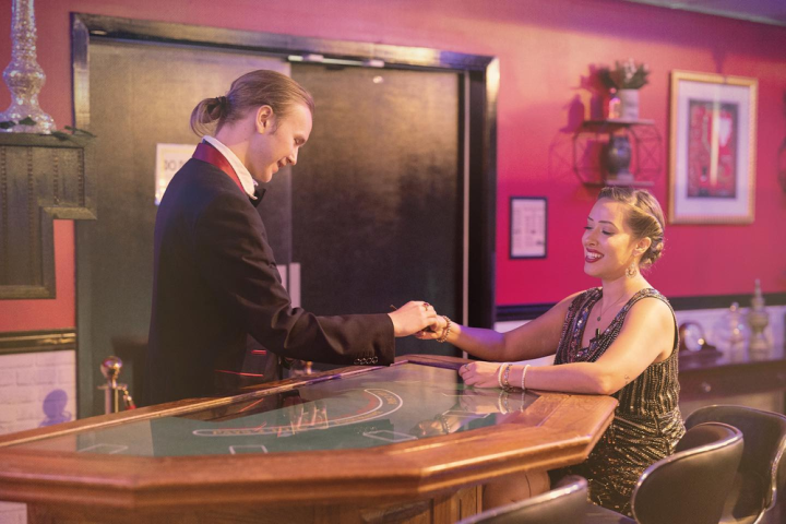 Man in suit shakes hand with smiling woman at casino table in warmly lit room.