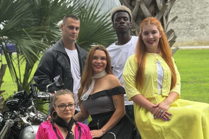Five people posing with a motorcycle near palm trees.